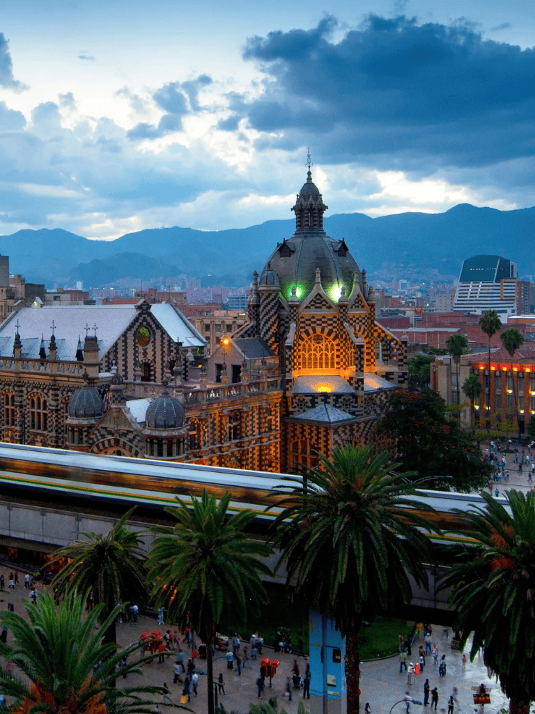 Colorful historic building with dome in cityscape, mountain background, palm trees, and crowds.