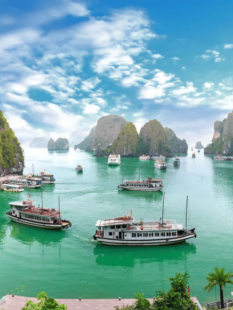 Colorful boats sailing on emerald waters surrounded by lush limestone islands in Halong Bay, Vietnam.