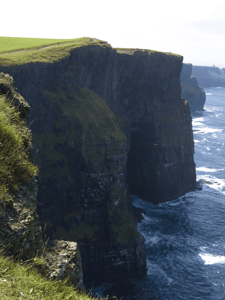 Stunning Cliffs of Moher in Ireland with lush green grass and crashing Atlantic Ocean waves.