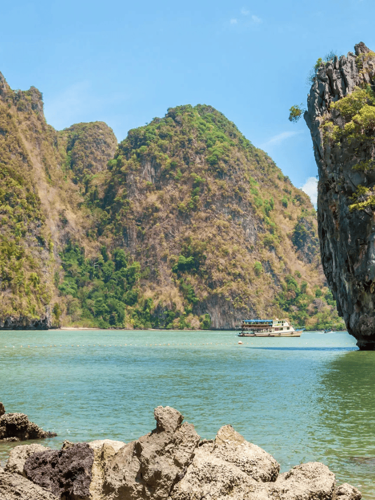 Stunning tropical bay with limestone cliffs and boat in clear blue waters.