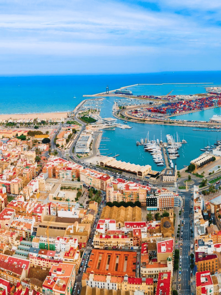 Aerial view of a vibrant coastal city with marina, harbor, and colorful buildings near the beach.