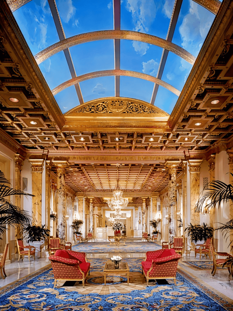 Luxurious hotel interior with ornate gold accents and high vaulted glass ceiling showing sky.