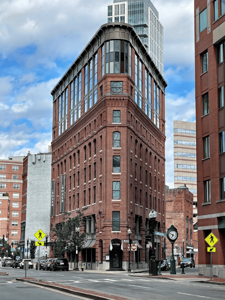 Historic brick building in downtown with modern glass addition, vibrant city street scene, and clear blue sky.