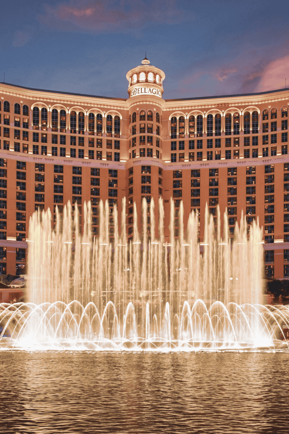 Luxurious Bellagio Hotel in Las Vegas with iconic fountain show at sunset.