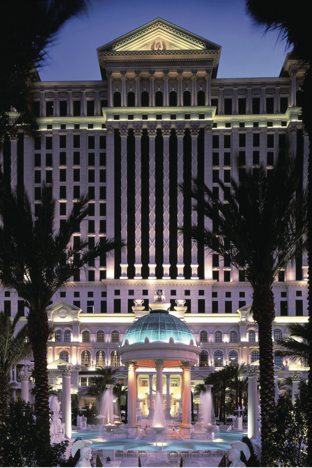 Luxurious hotel exterior at night with fountains and palm trees, illuminated for an elegant ambiance.