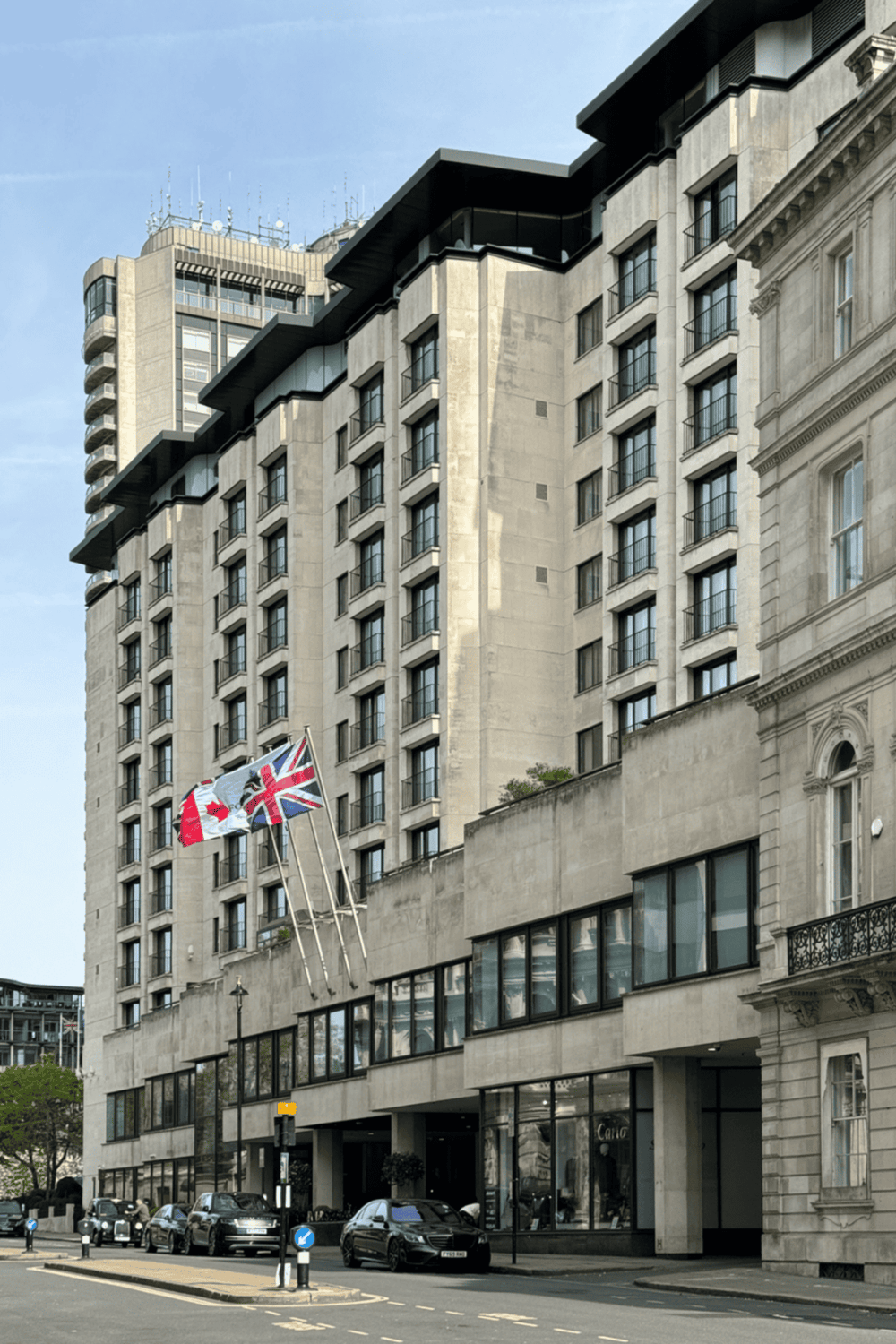 Luxurious hotel building with Union Jack flags in London, modern architecture on busy city street scene.