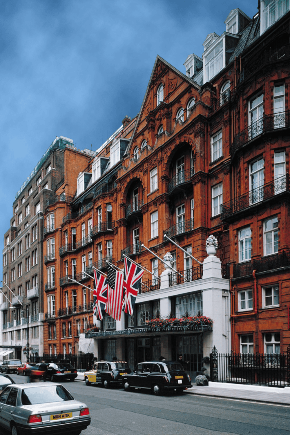 Luxurious hotel facade in London with British flags and vintage cars on the street.