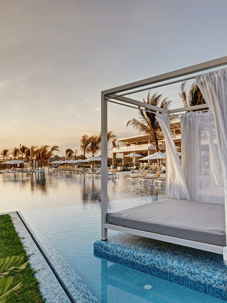 Luxurious poolside cabana at tropical beach resort with palm trees and sunset view.