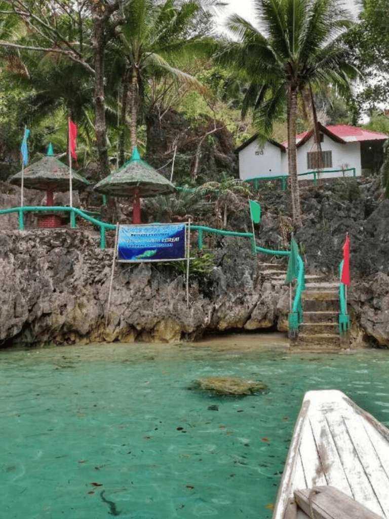 Relaxing tropical beach with palm trees, rocks, and small huts near clear turquoise water.