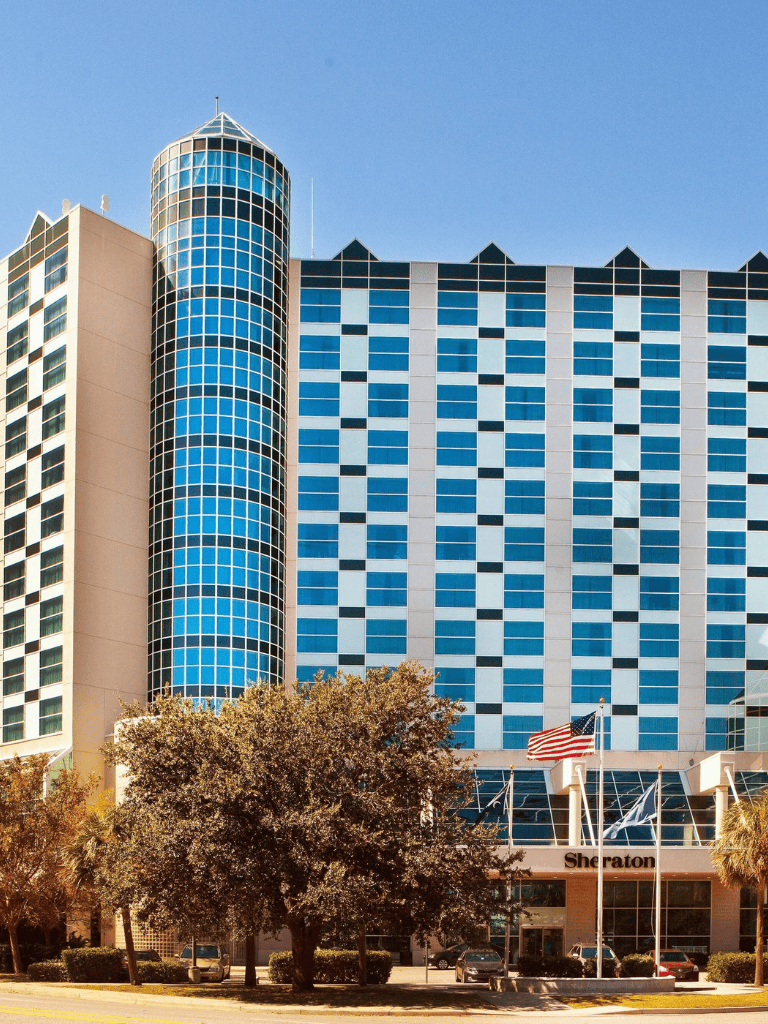 Modern downtown skyscraper with blue glass windows and Sheraton hotel entrance.