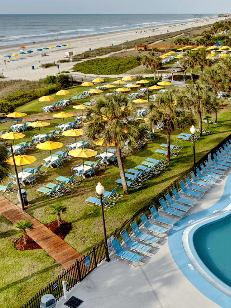 Beachside resort with swimming pool, lounge chairs, and colorful umbrellas on the sandy shoreline.