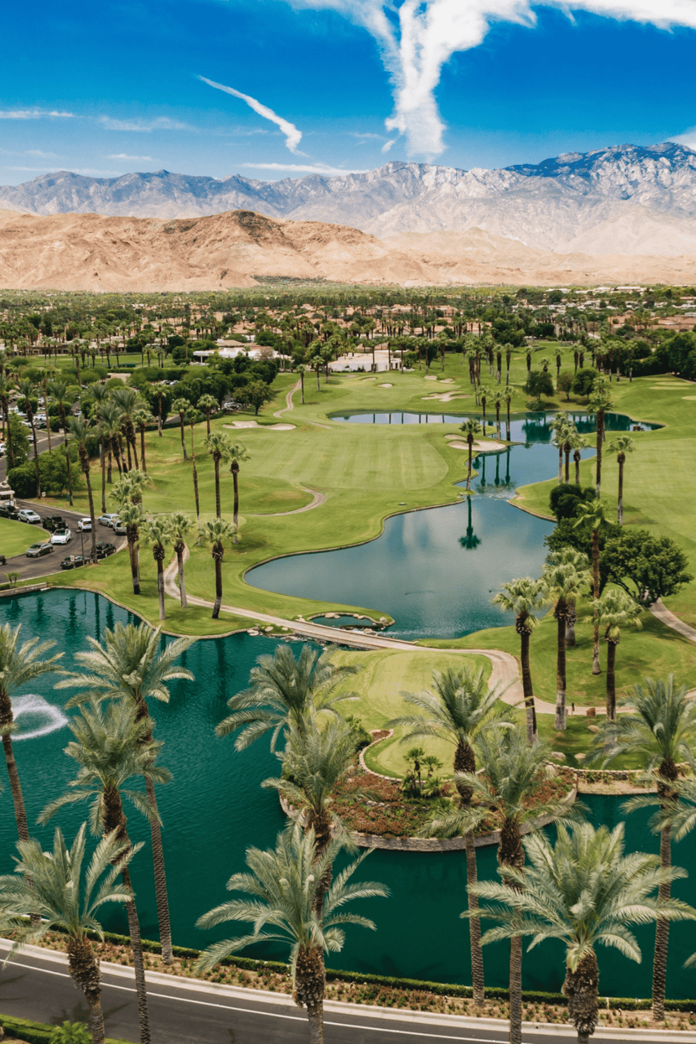 Lush desert golf course with lakes, palm trees, mountains, and clear blue sky in Palm Springs, California.
