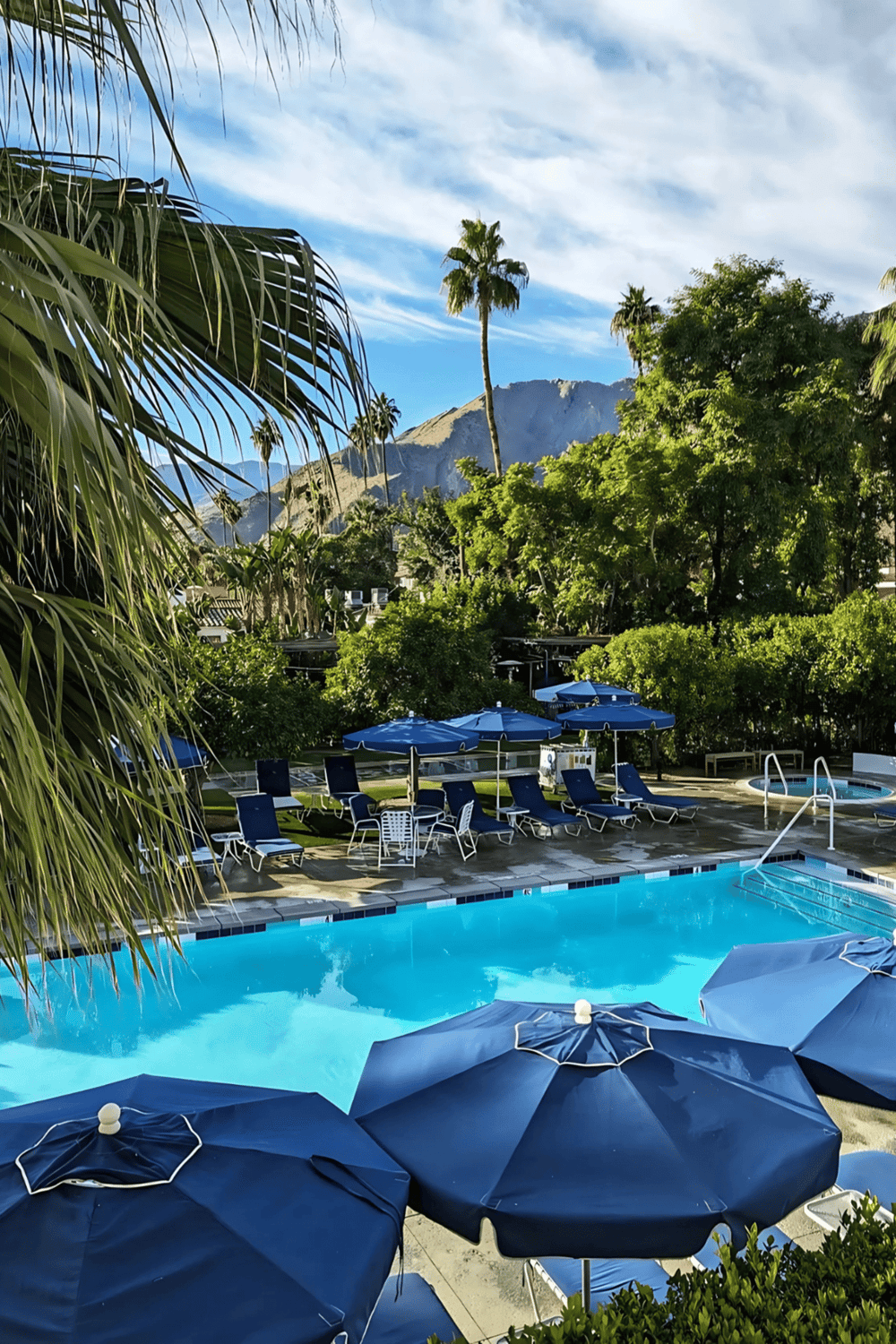 Relaxing outdoor swimming pool with blue umbrellas and lush greenery in a tropical resort setting.