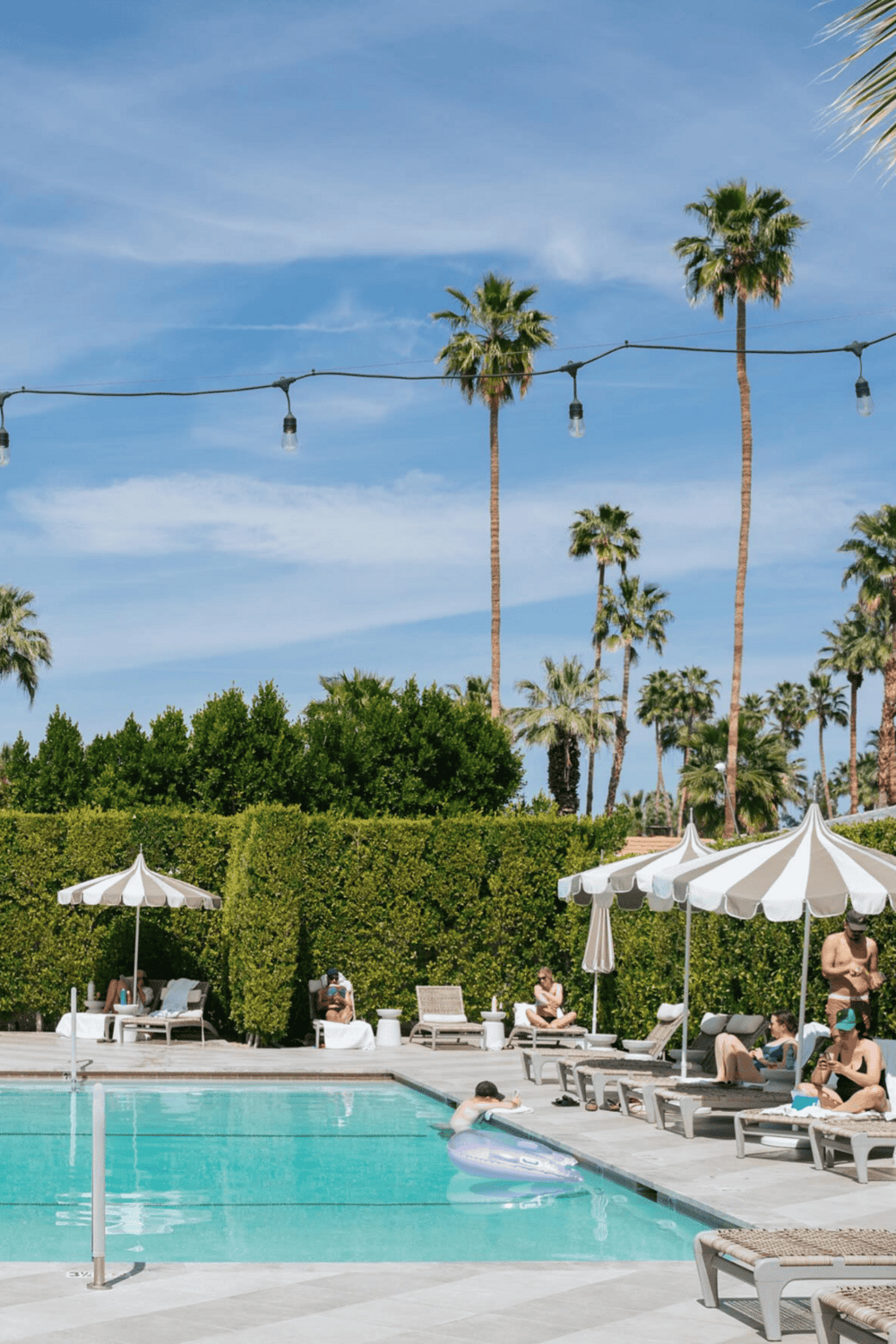 Relaxing poolside scene with palm trees, umbrellas, and people enjoying summer at luxury resort.