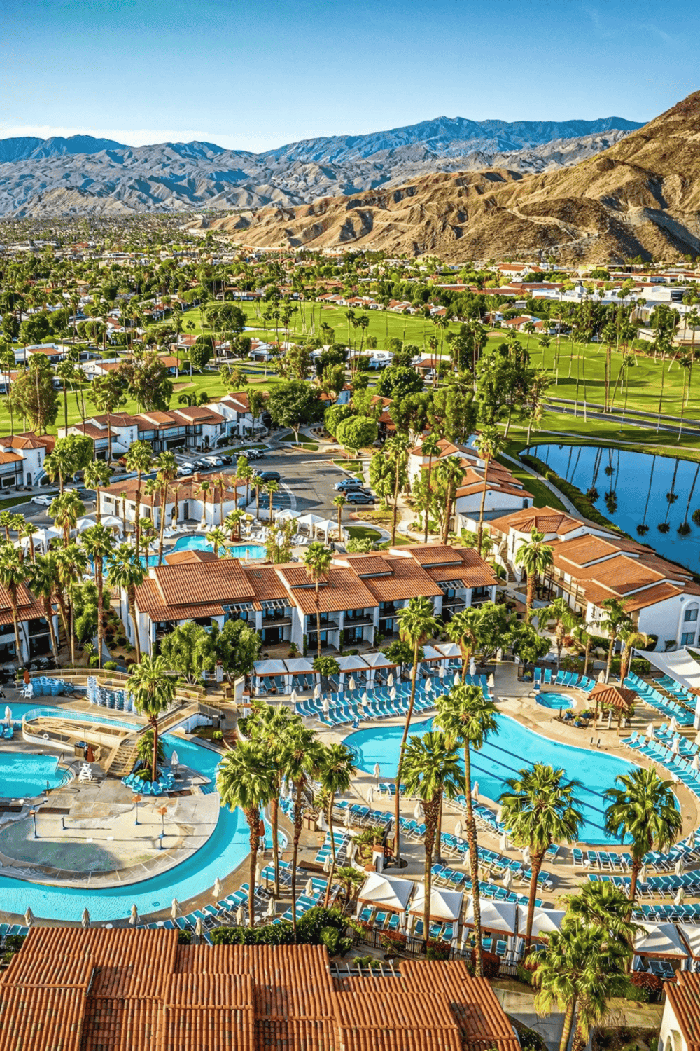 Sprawling resort with pools, lush greenery, mountains, and desert landscape in the background.