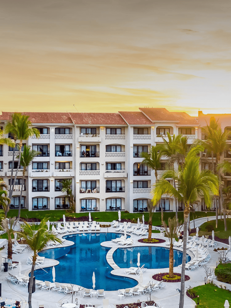Luxurious hotel pool with palm trees and modern architecture at sunset.