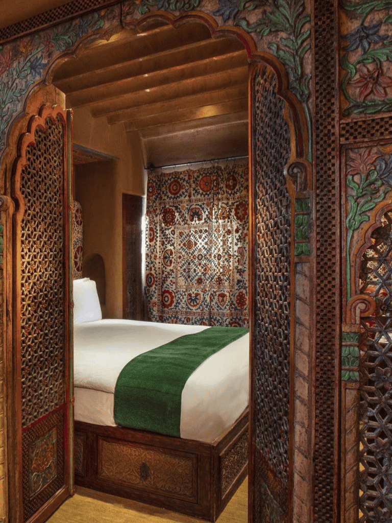 Intricate wooden lattice room divider in a traditionally decorated bedroom with vibrant textiles.