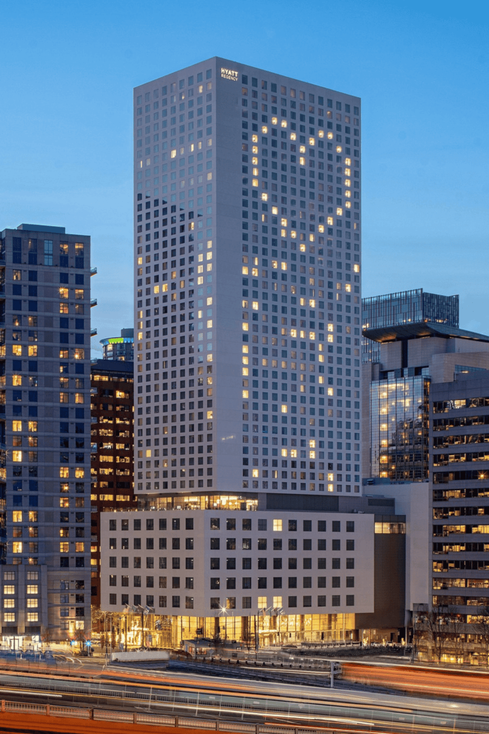 Modern city skyline with Hyatt Regency building featuring a heart-shaped light display at dusk.