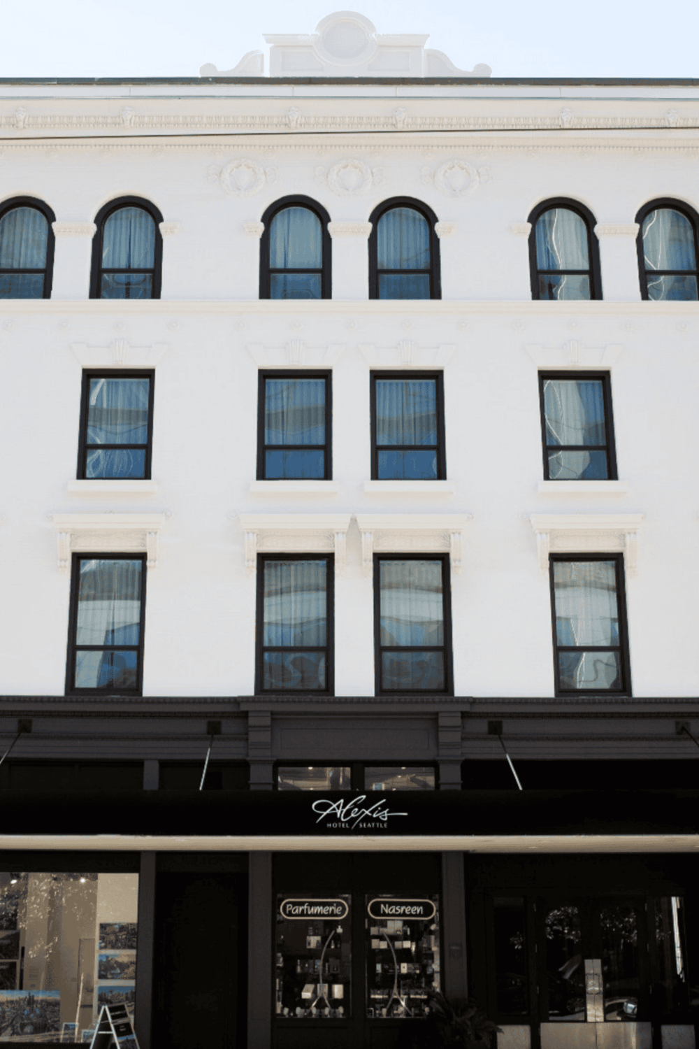 Elegant white building with arched windows and a stylish storefront for Alexis Hotel Seattle.