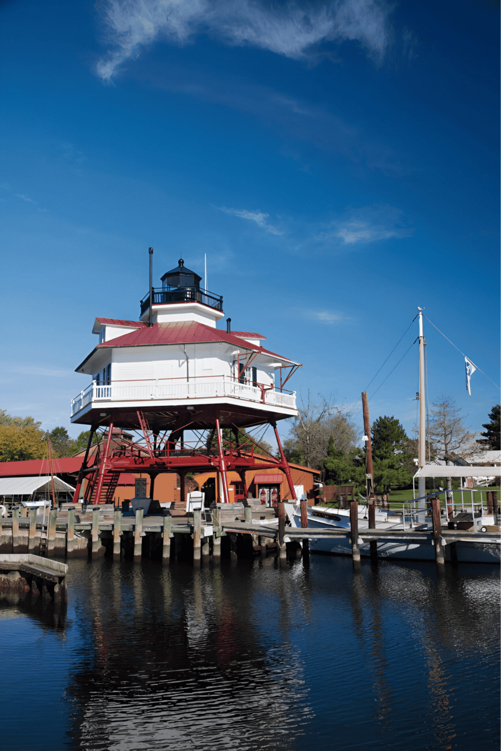 Lighthouse by the water with boats and dock, scenic coastal navigation landmark for travelers.