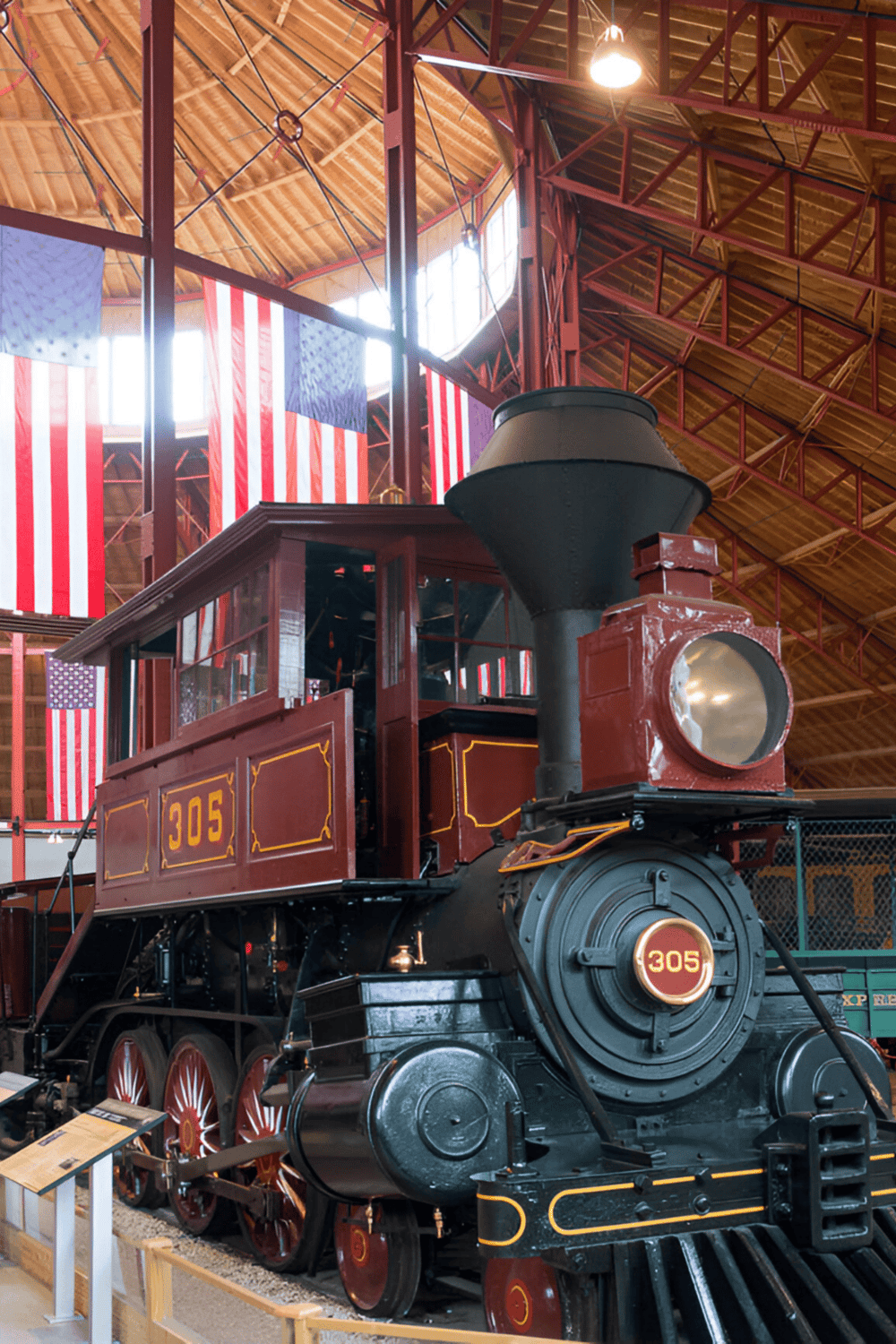 Steam locomobile train with American flags inside museum.