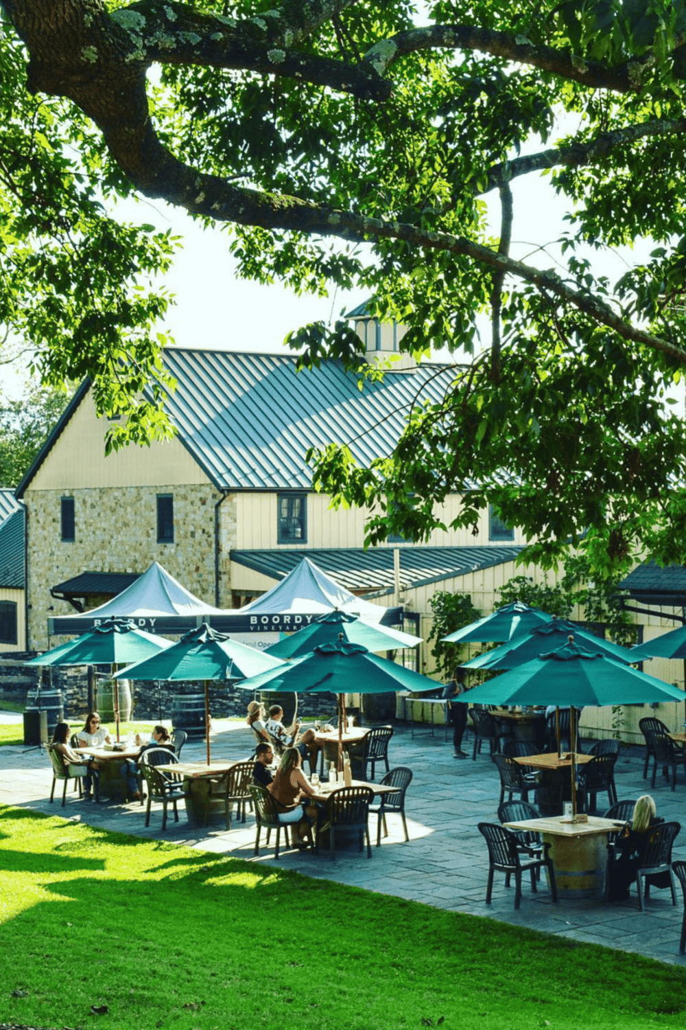 Outdoor wine tasting at Boordy Vineyards under green shade umbrellas, scenic historic building in background.