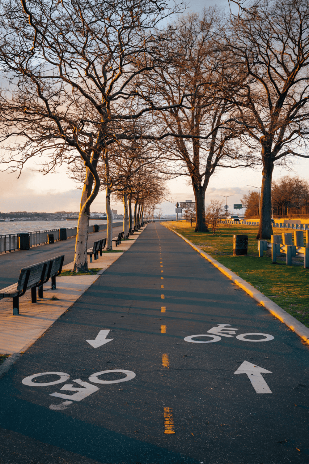 Bike lane on riverside promenade with trees, benches, and sunset sky, perfect for urban outdoor recreation.