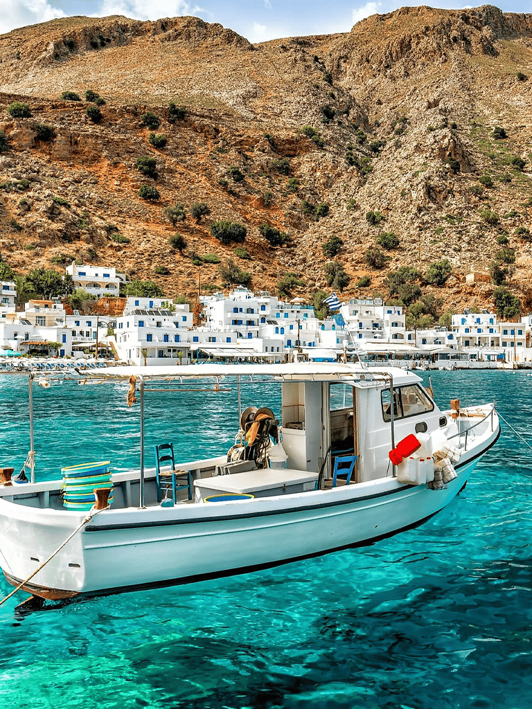Boat sailing in turquoise waters near a white Mediterranean town with hillside backdrop.