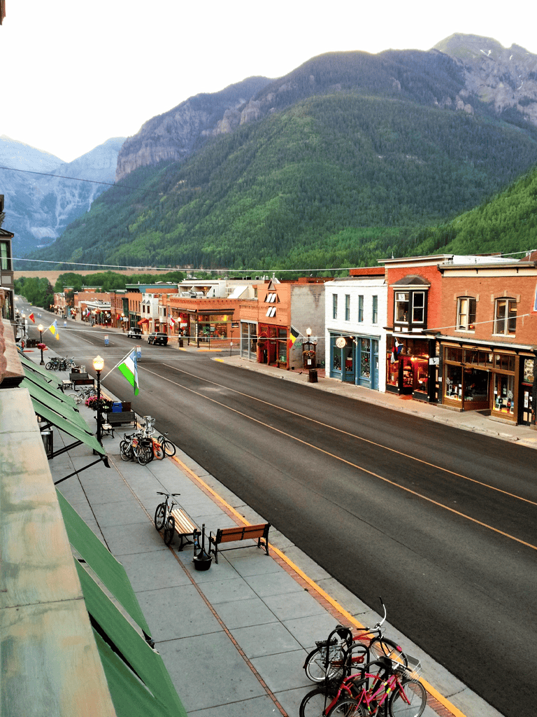 Bike racks with bicycles on a small-town street with colorful shops and mountain backdrop.