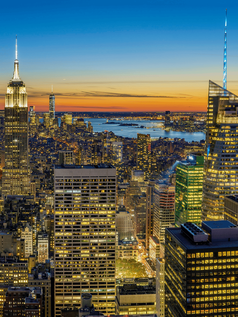 Breathtaking New York City skyline at sunset with illuminated skyscrapers and iconic Empire State Building, urban cityscape scene.