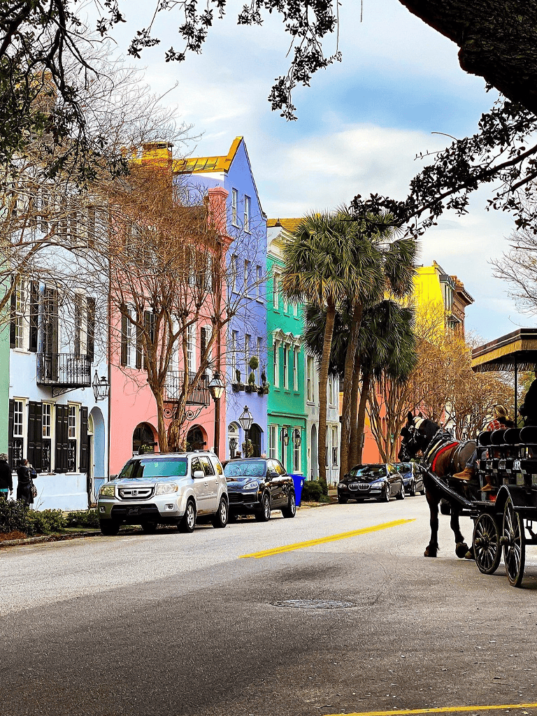 Colorful houses on a scenic street with parked cars and horse carriage in Charleston, South Carolina.