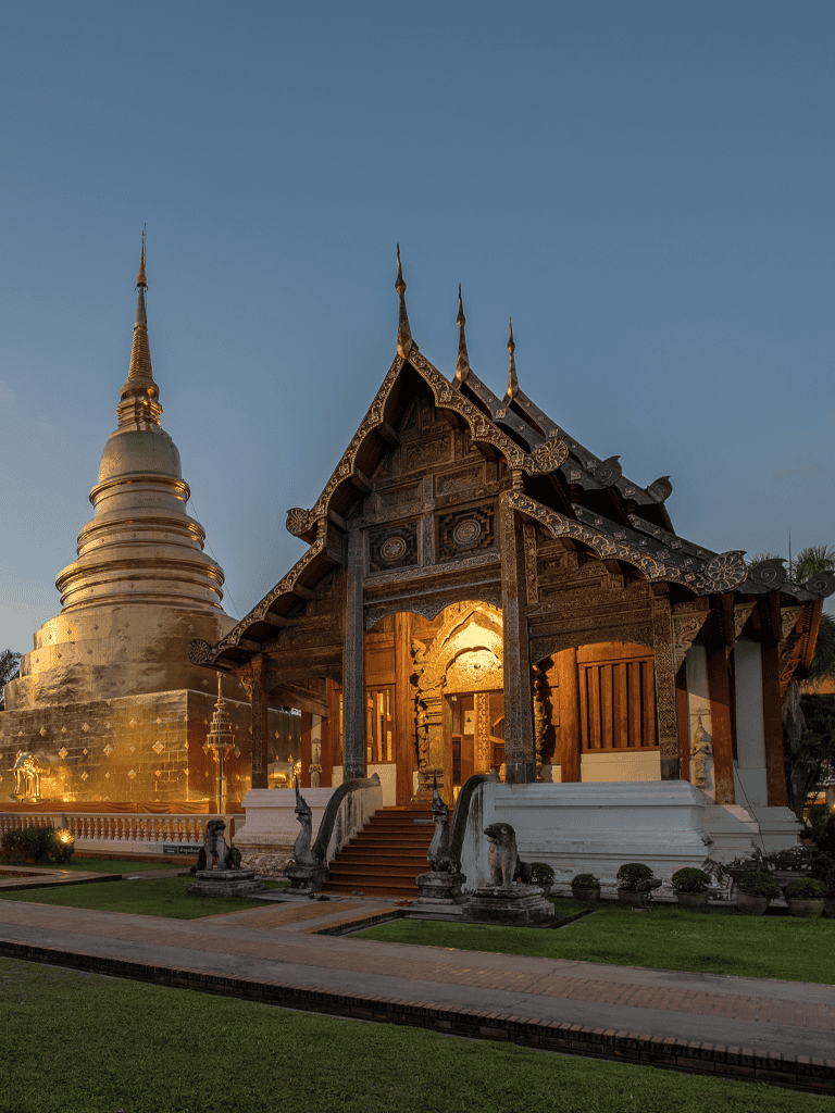 Ancient Thai temple with ornate wooden architecture and golden stupa at sunset.