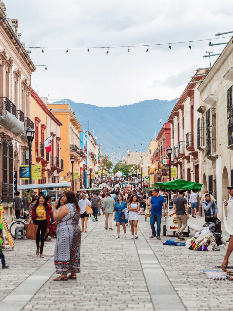 Colorful street in a vibrant town, crowded with pedestrians and local vendors, mountain backdrop.