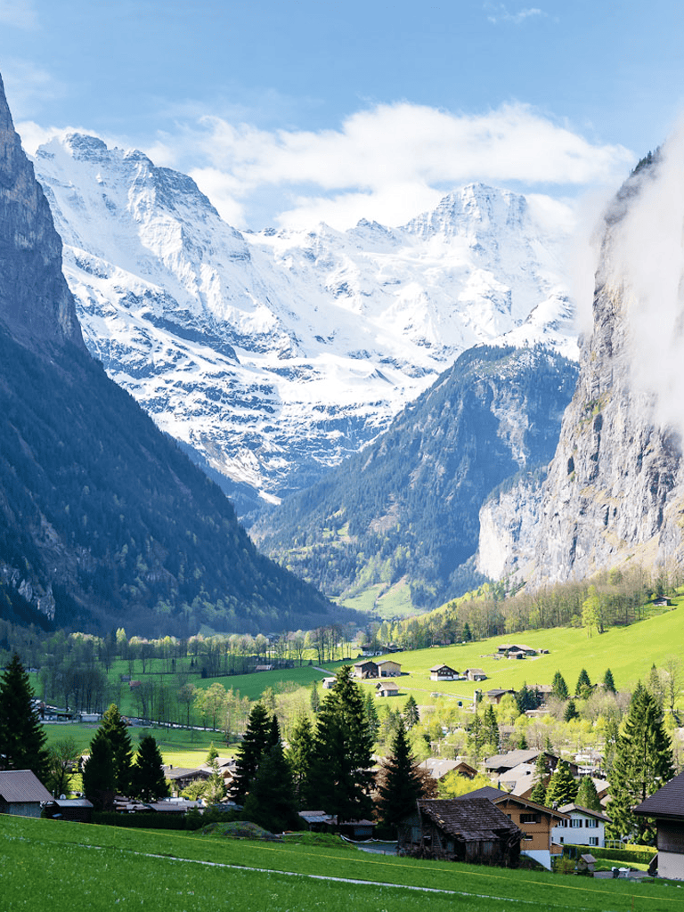 Snow-capped mountain landscape with green valley and village, serene Swiss Alps scenery.