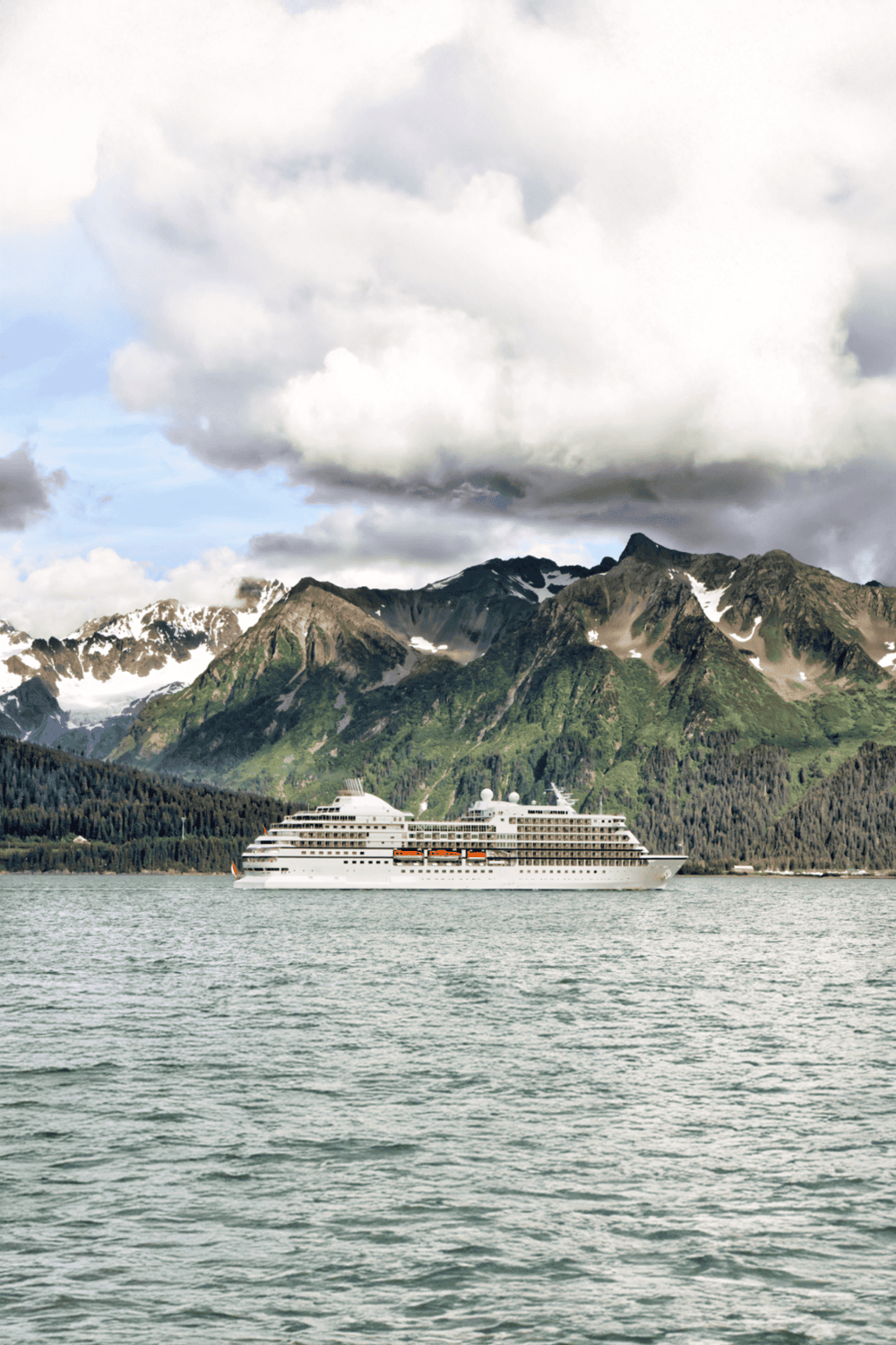 Cruise ship sailing in scenic mountain fjord with lush green peaks and cloudy sky.