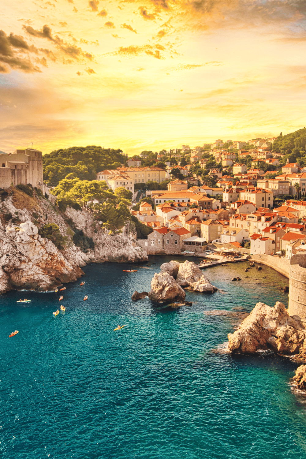 Cliffside Croatian coastal town with colorful houses and turquoise waters at sunset.