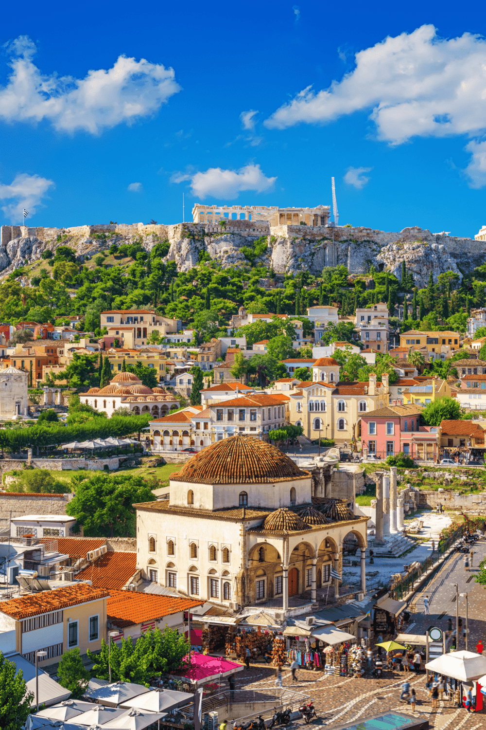 Ancient Acropolis and historic cityscape of Athens, Greece, with vibrant buildings under a bright blue sky.