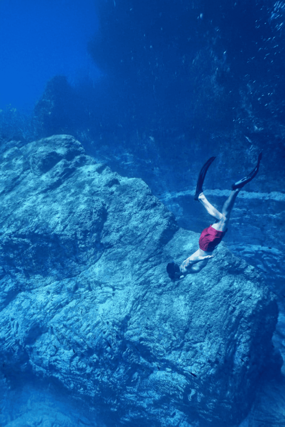 Underwater scuba diver exploring rocky ocean floor in clear blue water.