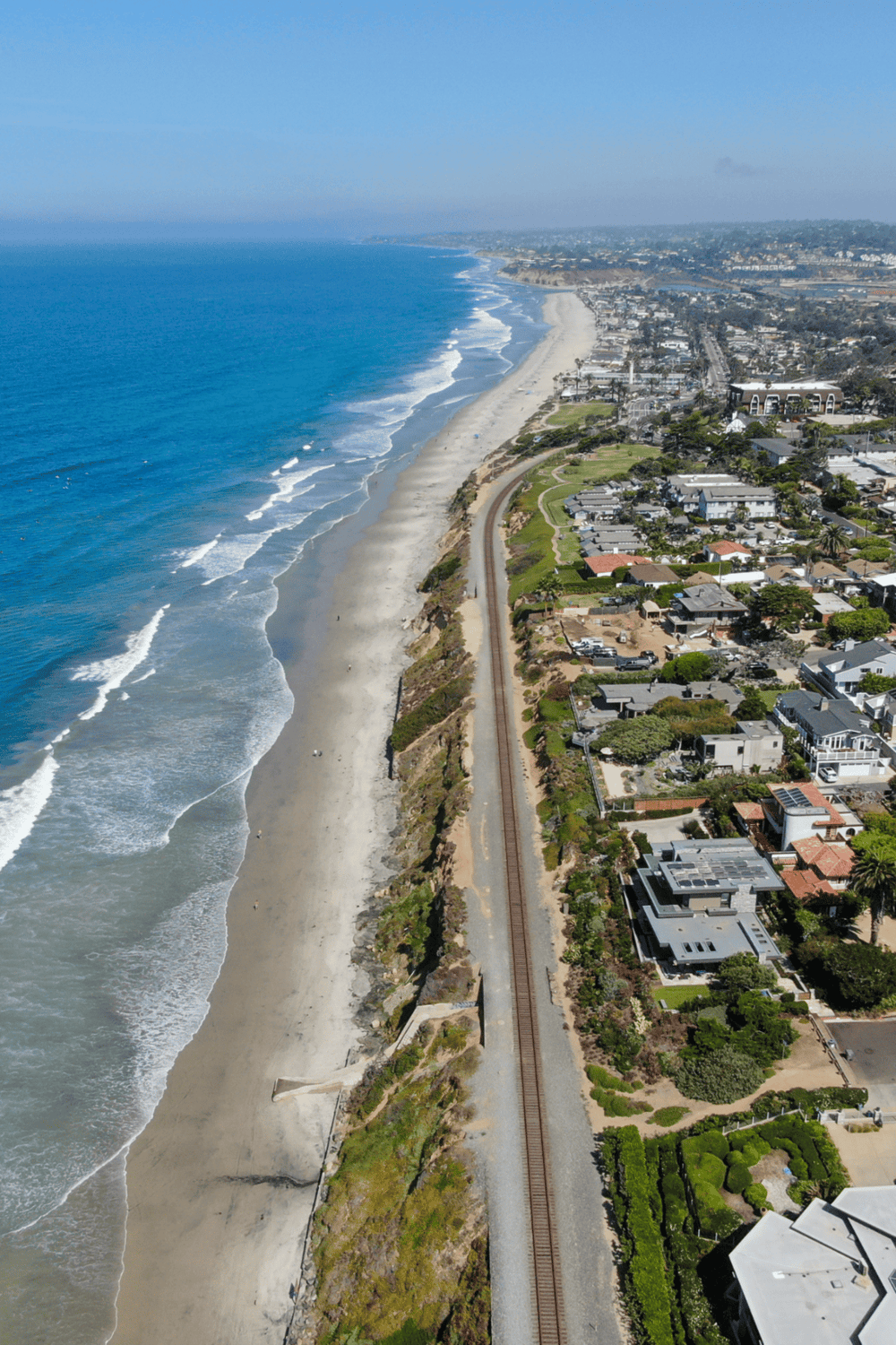 Breathtaking aerial view of the California coast with ocean waves, sandy beaches, and coastal residential neighborhoods.