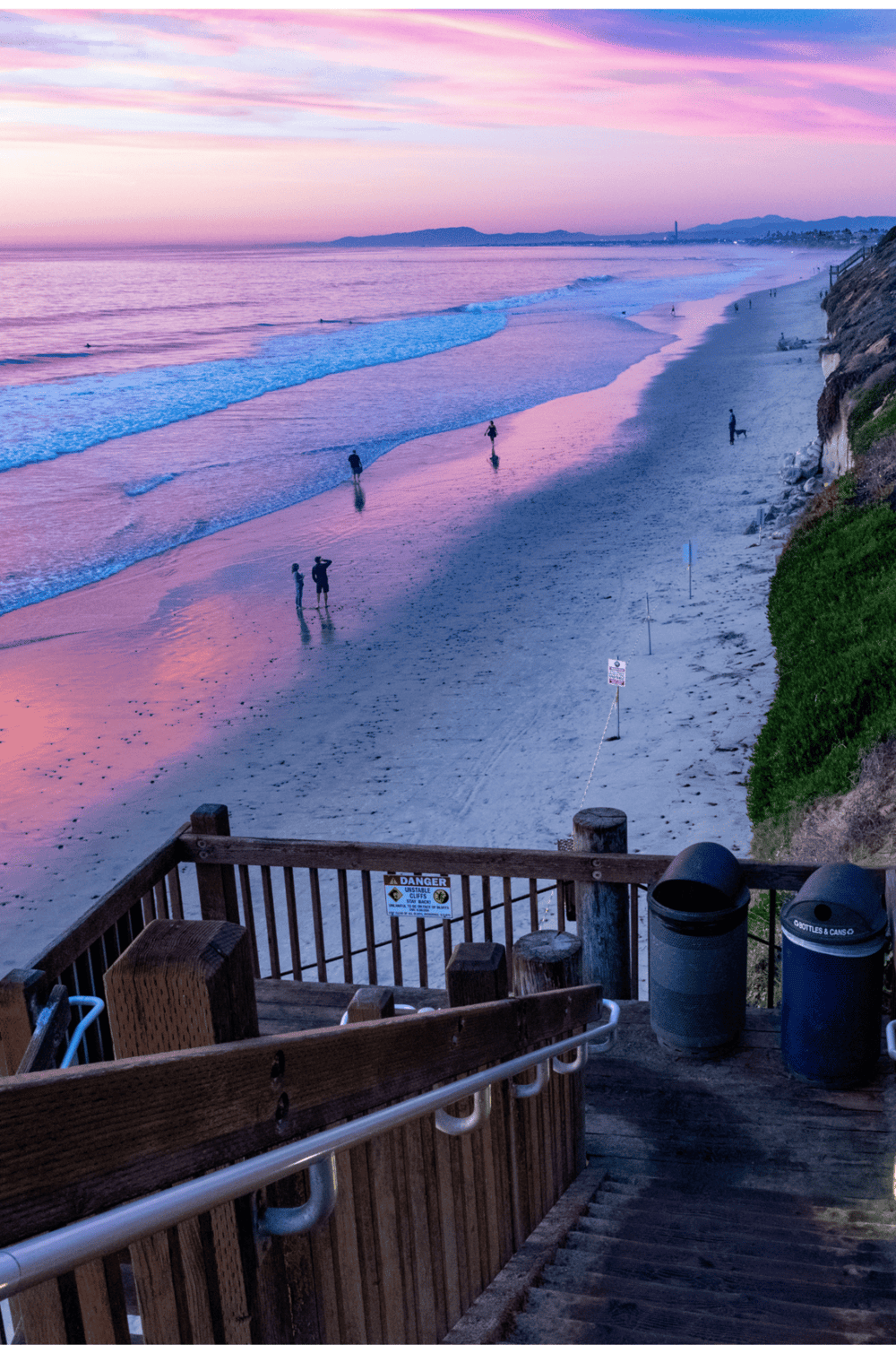Aerial view of a scenic beach at sunset with people walking, surfing, and relaxing along the shoreline.