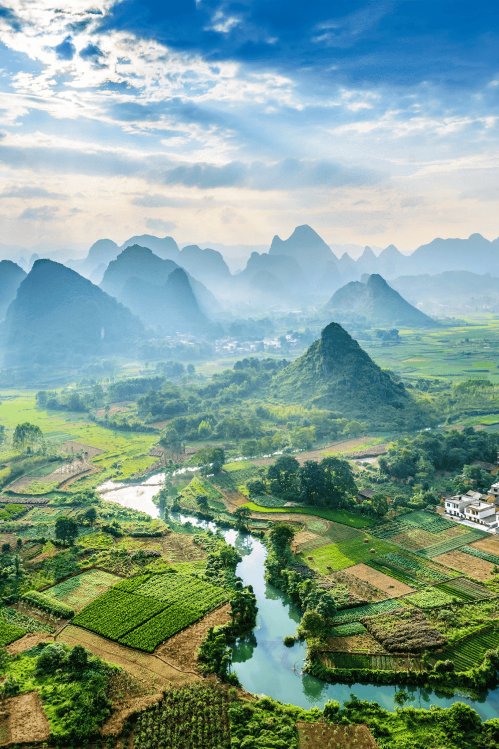 Lush green landscape with karst mountains, river, farmland, and rural village in Vietnam.