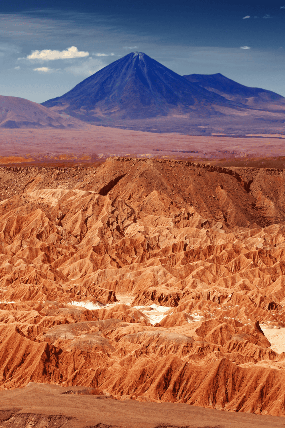 Vibrant desert landscape with rugged red rocks and Mount Etna in the background.