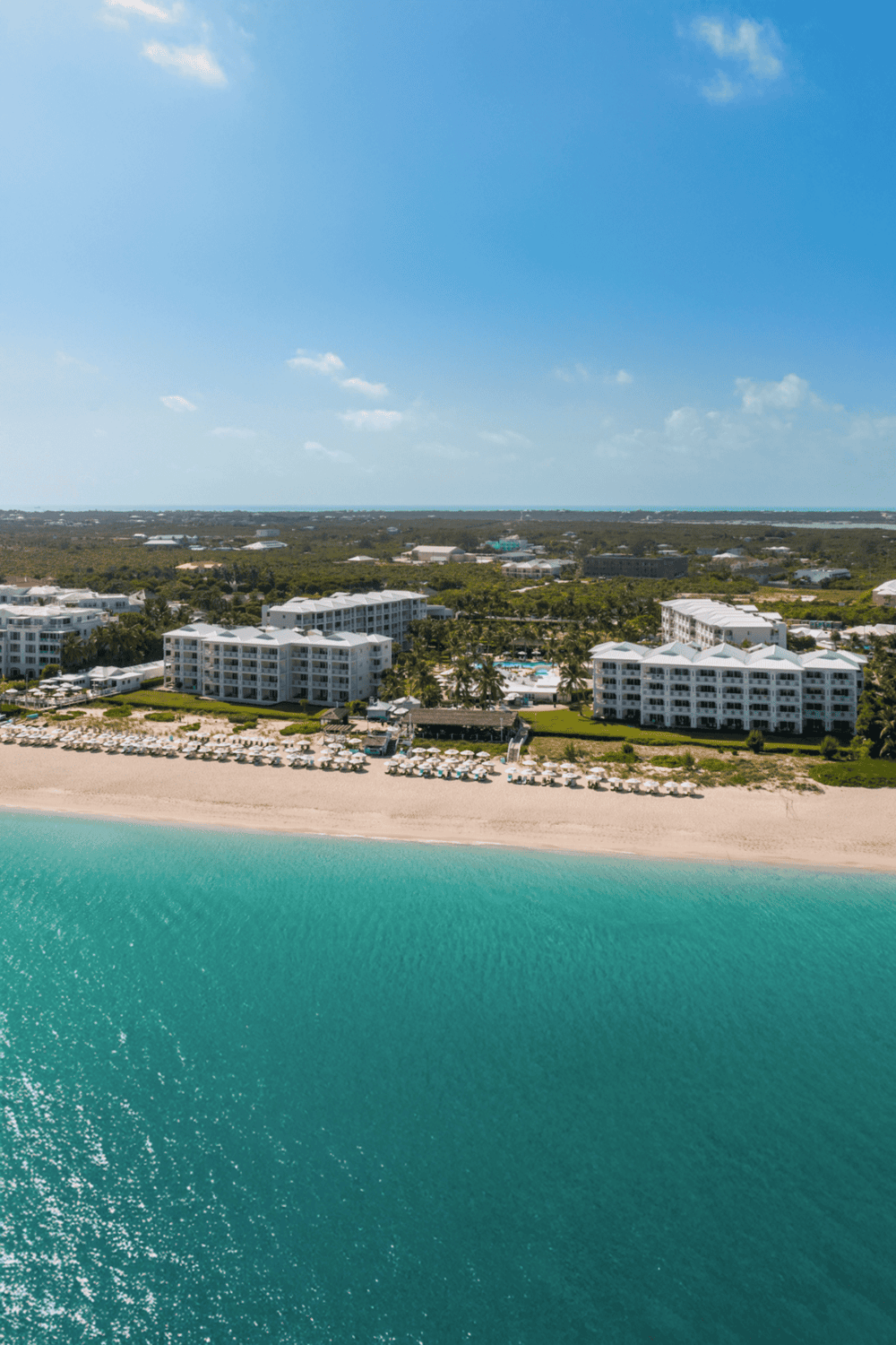 Oceanfront resort with white buildings, sandy beach, and clear turquoise water, perfect for tropical vacations.