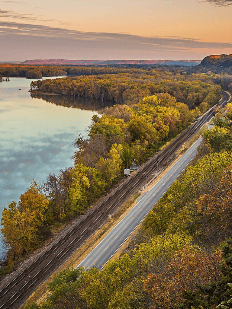 Vibrant fall foliage along a scenic riverside railway and road at sunset.