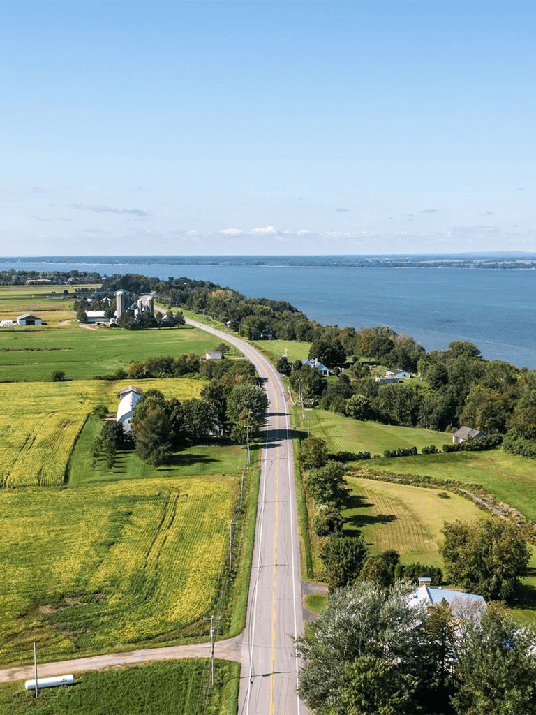Serene rural landscape with lake, open fields, and country road, perfect for scenic travel routes.