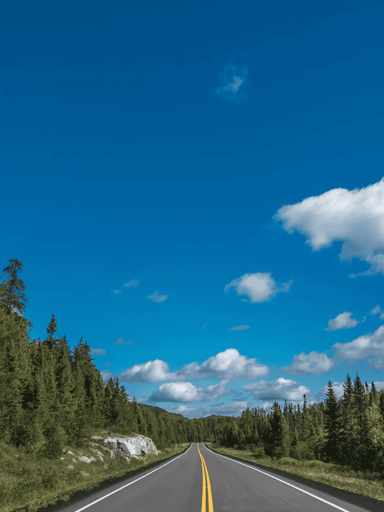 Open road through lush forest under blue sky with clouds, scenic drive, travel destination, nature, adventure, road trip, outdoor exploration, QuestForDirections.