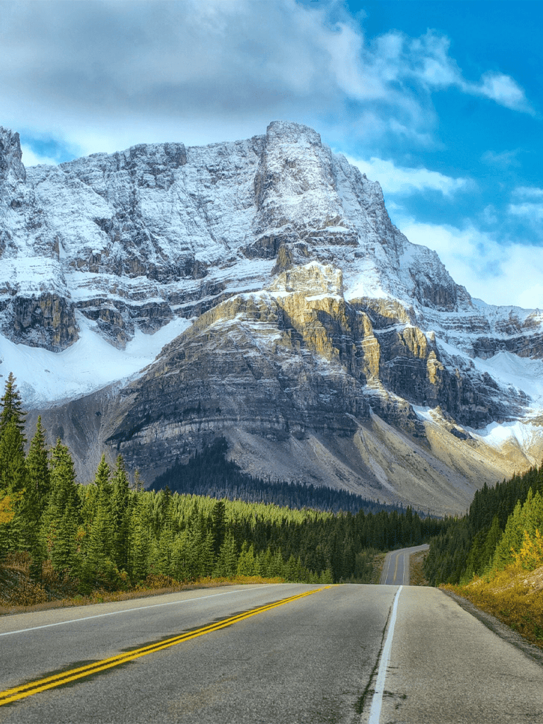 Snow-capped mountain landscape with highway and pine trees in Alberta, Canada.