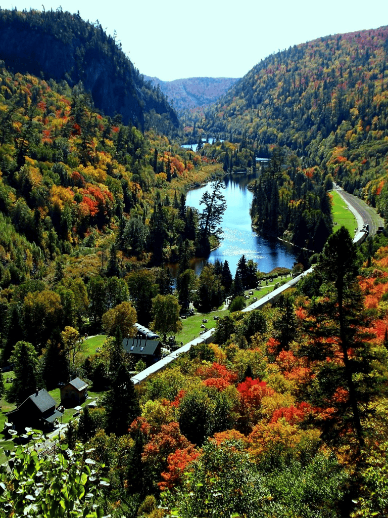 Vibrant autumn landscape with colorful trees, river, and mountains in the background, showcasing scenic outdoor travel destinations.
