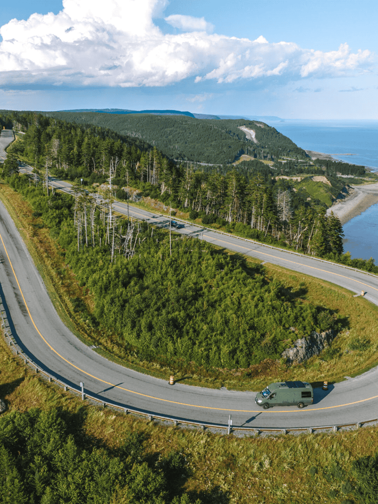 Scenic coastal winding road with lush green forest and ocean views in the background.