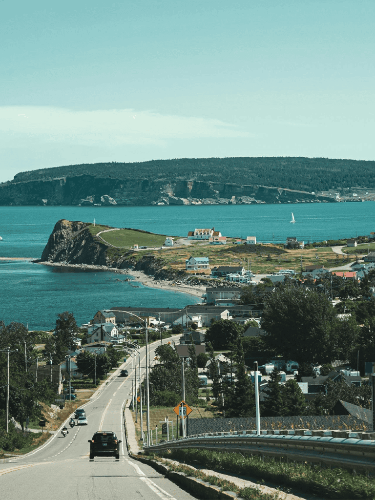 Scenic coastal road heading to island with houses and ocean views, travel guide to Atlantic Canada.